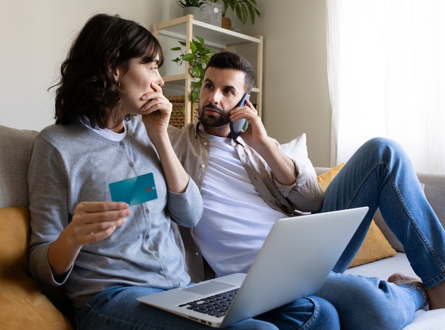 A couple on a sofa with a laptop and a credit card, reviewing tips to avoid identity theft on vacation